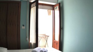 Habitación de hotel con dos camas, una lámpara en el techo, un equipo de aire acondicionado y vista al exterior por una puerta abierta.