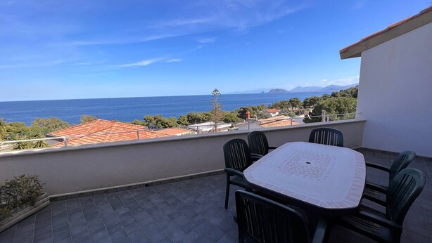 Un balcón con mesa y sillas, con vistas a la costa, edificios y montañas al fondo.