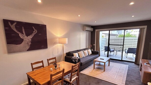 A modern living room with a dining area, a sofa, and a large window. - Relaxing Oasis in Bruce -1bd Apt (Bruce)
