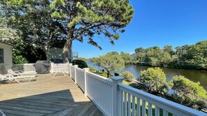 Une terrasse en bois avec des balustrades blanches, des meubles d’extérieur et une vue sur une rivière.