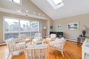 A spacious living room with large windows, a piano, and a round coffee table.