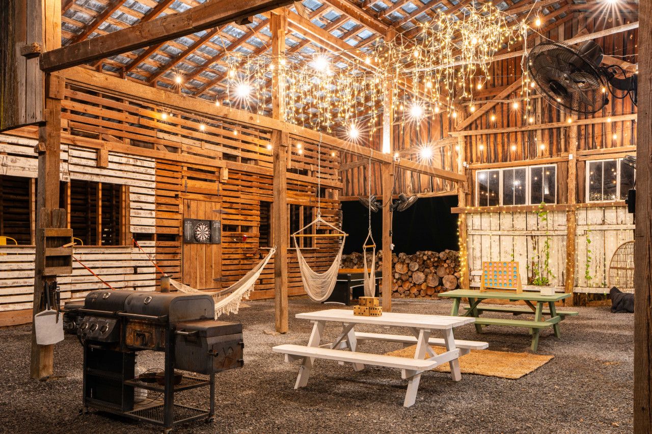 Un interior rústico de madera con techo alto, vigas de madera, una hamaca, mesas de picnic y una parrilla.