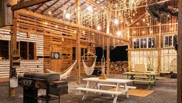 Un interior rústico de madera con techo alto, vigas de madera, una hamaca, mesas de picnic y una parrilla.
