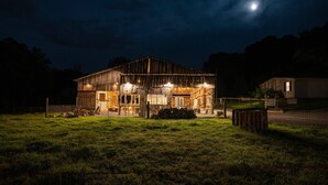 Ein rustikales Gebäude im Stil eines Bauernhauses mit großem offenen Vorderbereich, möglicherweise ein Stall oder eine Werkstatt, umgeben von einem eingezäunten Hof.
