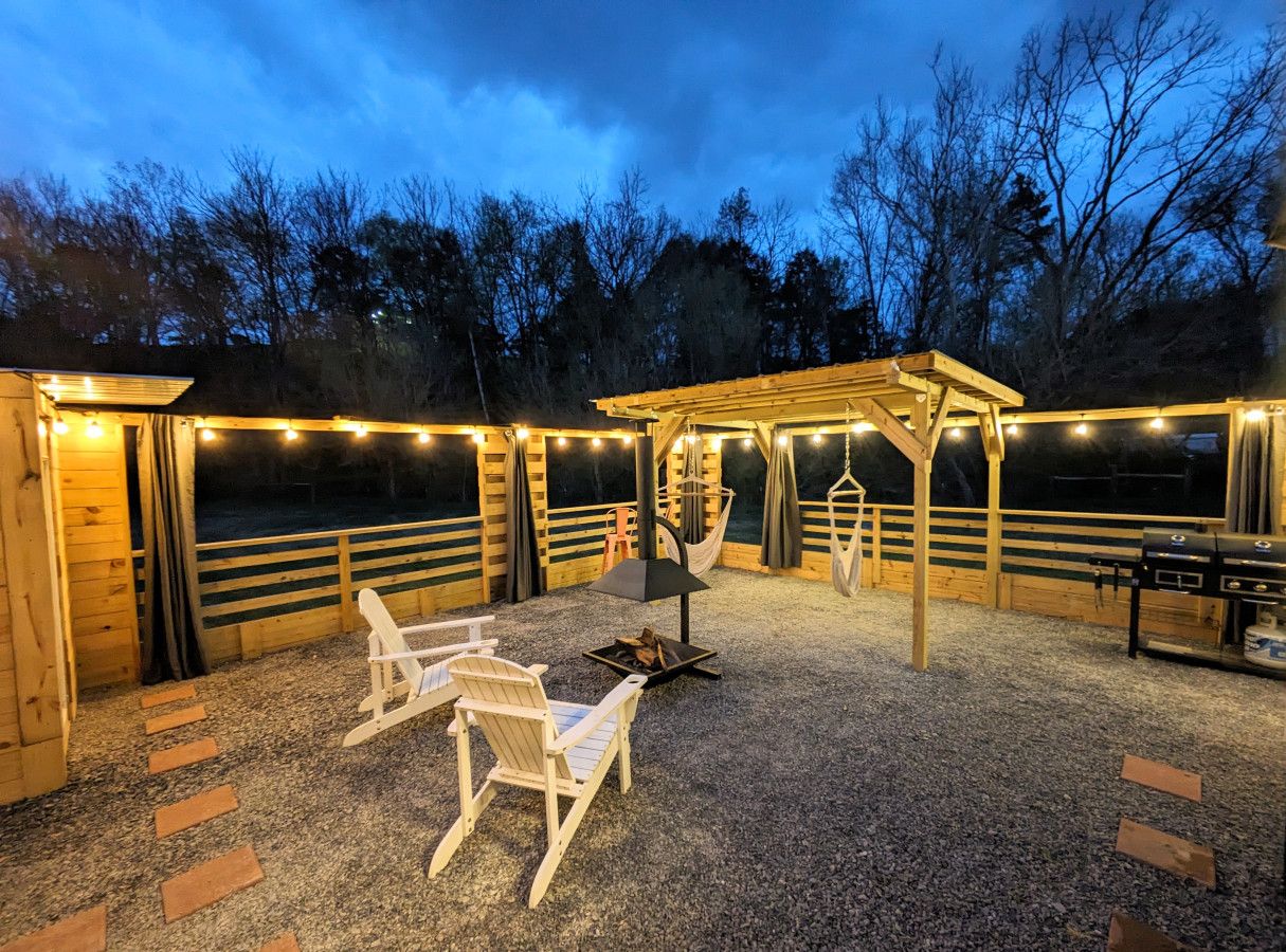 Un patio al aire libre con muebles de madera, una parrilla y luces colgantes.
