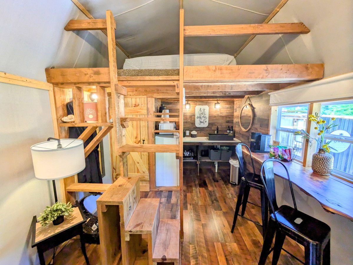 Una habitación compacta y rústica estilo cabaña, con cama en altillo, muebles de madera, kitchenette y ventana con vistas.