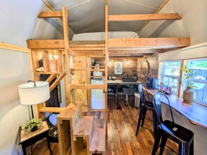 Una habitación compacta y rústica estilo cabaña, con cama en altillo, muebles de madera, kitchenette y ventana con vistas.