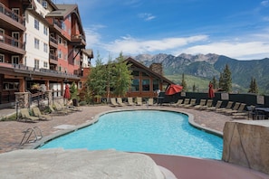 A pool area with lounge chairs and a view of mountains.