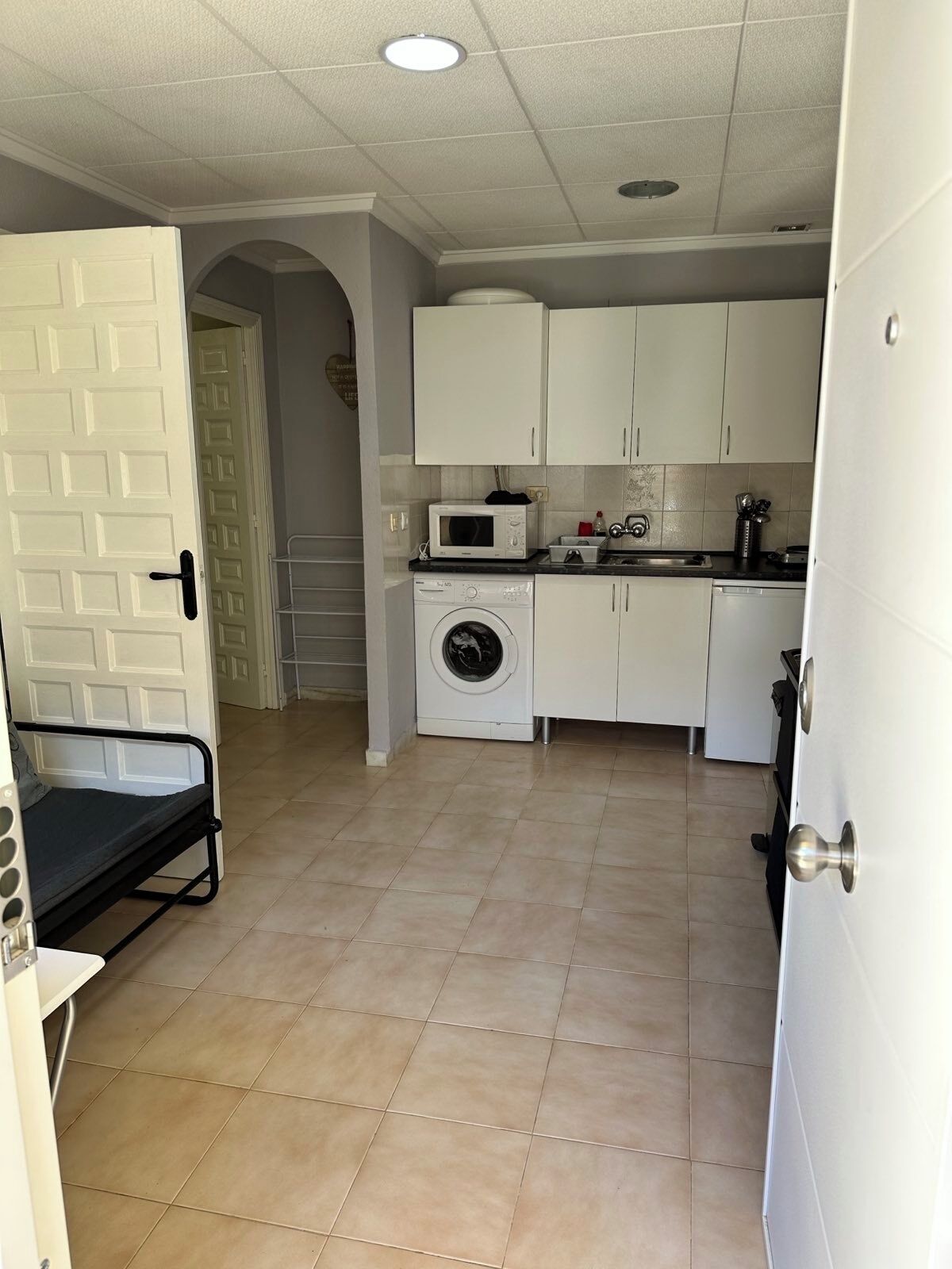 A compact kitchen with white cabinets, a microwave, a washing machine, and a sink.