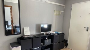 Una habitación de hotel moderna con una mesa consola negra, un televisor de pantalla plana, un pequeño cubo de basura y una puerta blanca.