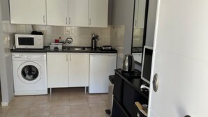 Una cocina compacta con armarios blancos, microondas, lavadora y estufa.