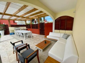 Un espace extérieur aménagé en terrasse, avec un canapé blanc, des chaises en bois, une table à manger et une table basse.