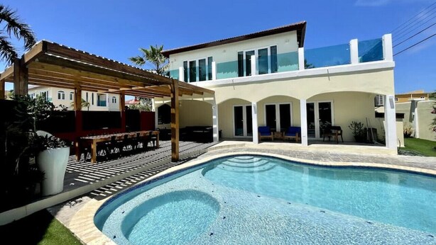 Ein modernes Haus mit Schwimmbad, überdachter Terrasse und einem gepflegten Garten.