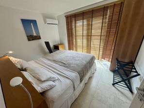Une chambre à coucher avec un lit, une table de chevet, une lampe, un tableau au mur et une fenêtre avec des stores.