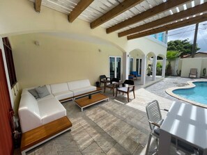 Un espace de vie extérieur abrité, doté d’une piscine, d’un canapé blanc, d’une table basse en bois et de chaises d’extérieur.