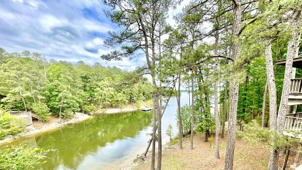 A riverside view with a wooden deck, surrounded by trees and a clear sky. - 80BPD, Four bedroom, two 1/2 bath log-sided condo with lake view , garage by RedAwning (Mount Ida)