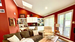 A living room with a sectional sofa, a coffee table, and a patterned rug. There is a kitchen area with white cabinets and a dining table with chairs. - 80BPD, Four bedroom, two 1/2 bath log-sided condo with lake view , garage by RedAwning (Mount Ida)