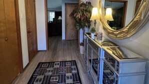 A hallway with a patterned rug, a large mirror, a lamp, and a ceiling light fixture. - Forest view, log-sided two bedroom, two bath condo on Lake Ouachita. by RedAwning (Mount Ida)
