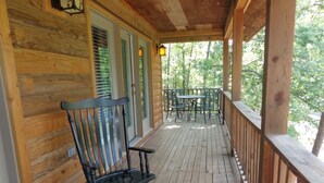 A wooden porch with a rocking chair and a table, overlooking a wooded area. - Forest view, log-sided two bedroom, two bath condo on Lake Ouachita. by RedAwning (Mount Ida)