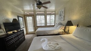 Quarto de hotel com duas camas, um ventilador de teto, uma televisão sobre uma cômoda e uma janela com persianas.