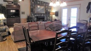 A dining area with a stone fireplace, a chandelier, and a television. - Lake view three bedroom, three bath cottage with private hot tub overlooking Lake Ouachita. by RedAwning (Mount Ida)