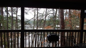A covered outdoor area with a grill and chairs, overlooking a forested area and a body of water. - Lake view three bedroom, three bath cottage with private hot tub overlooking Lake Ouachita. by RedAwning (Mount Ida)