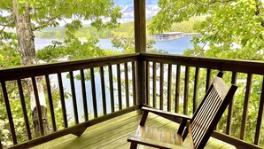 Um deck de madeira com um banco, com vista para um lago e uma ponte.