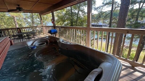 A hot tub on a wooden deck with a view of trees and a grill in the background. - Lake view two bedroom, two bath log-sided cottage with private hot tub overlooking Lake Ouachita. by RedAwning (Mount Ida)