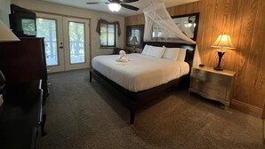 A bedroom with a bed, a ceiling fan, a nightstand, a lamp, and a wooden wall. - Lake view two bedroom, two bath log-sided cottage with private hot tub overlooking Lake Ouachita. by RedAwning (Mount Ida)
