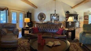 A traditional living room with a fireplace, leather furniture, and a chandelier. - Lake view two bedroom, two bath log-sided cottage with private hot tub overlooking Lake Ouachita. by RedAwning (Mount Ida)