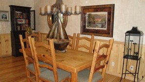 A dining room with a wooden table and chairs, a chandelier, a bookshelf, and a framed picture on the wall. - Lake view two bedroom, two bath log-sided cottage with private hot tub overlooking Lake Ouachita. by RedAwning (Mount Ida)