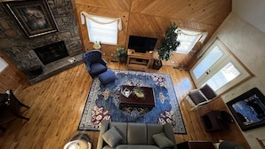 A cozy living room with a stone fireplace, a blue armchair, a grey sofa, and a coffee table with a decorative centerpiece. - Lake view two bedroom, two bath loft, log-sided cottage with private hot tub overlooking Lake Ouachita. by RedAwning (Mount Ida)