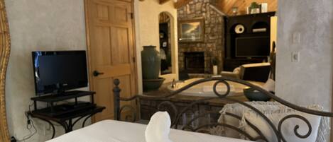 A bedroom with a bed, a television on a stand, a wooden door, and a stone wall.