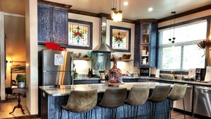 A modern kitchen with a central island, bar stools, and a large window with decorative stained glass. - Magnificent Four Bedroom, Two 1/2 Bath luxury, log-sided Harbor North cottage with incredible views of Lake Ouachita. by RedAwning (Mount Ida)