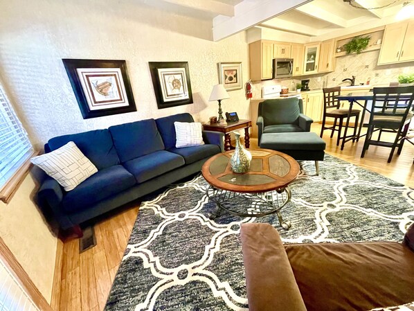 Uma sala de estar com um sofá azul, uma mesa de centro e um tapete estampado.