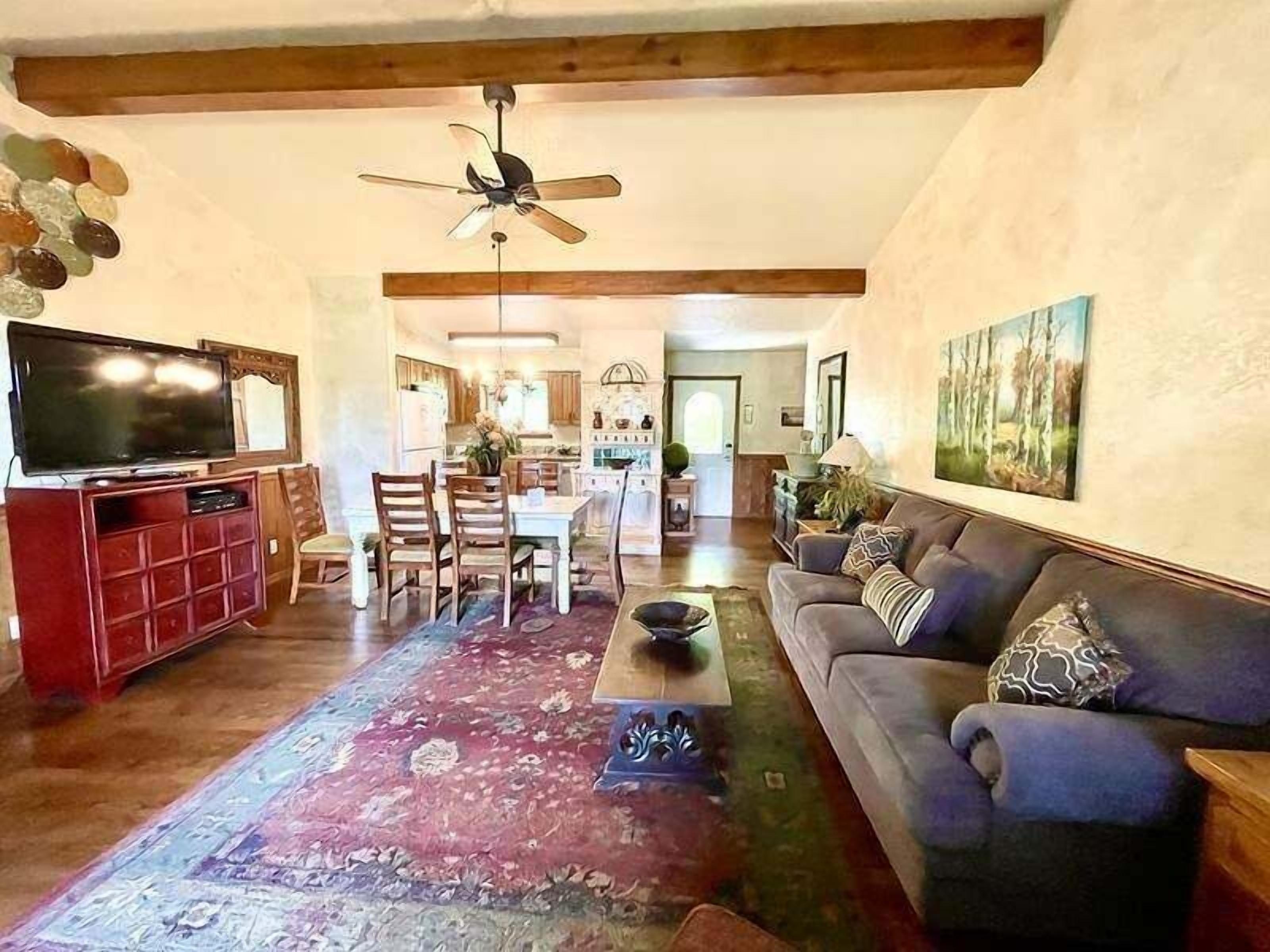 A spacious living room with a large TV, a blue sofa, a wooden ceiling, and a dining area in the background.