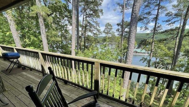 A wooden deck with a bench and a grill, overlooking a lake and forested area. - C8, Two bedroom, two bath log-sided, lake view luxury cottage with hot tub by RedAwning (Mount Ida)