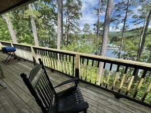 A wooden deck with a bench and a grill, overlooking a lake and forested area. - C8, Two bedroom, two bath log-sided, lake view luxury cottage with hot tub by RedAwning (Mount Ida)