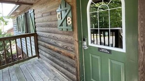 A wooden cabin with a green door, a small window with a white frame, and a wooden railing on the porch. - C8, Two bedroom, two bath log-sided, lake view luxury cottage with hot tub by RedAwning (Mount Ida)