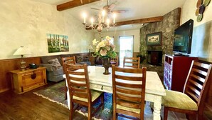 A dining area with a wooden table, chairs, a chandelier, and a stone fireplace. - C8, Two bedroom, two bath log-sided, lake view luxury cottage with hot tub by RedAwning (Mount Ida)