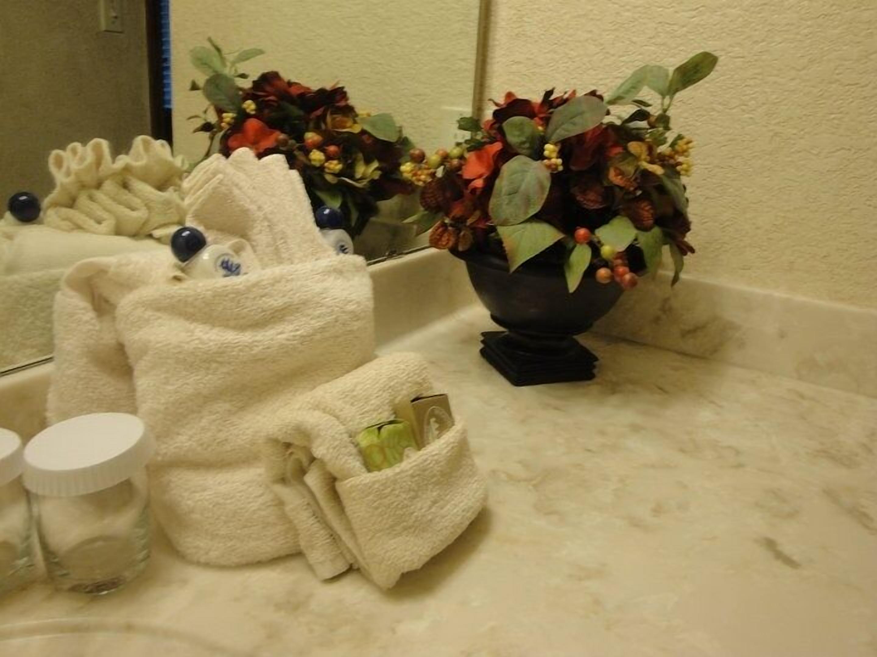 A bathroom with a white towel, a bottle, and a vase with flowers on the counter.