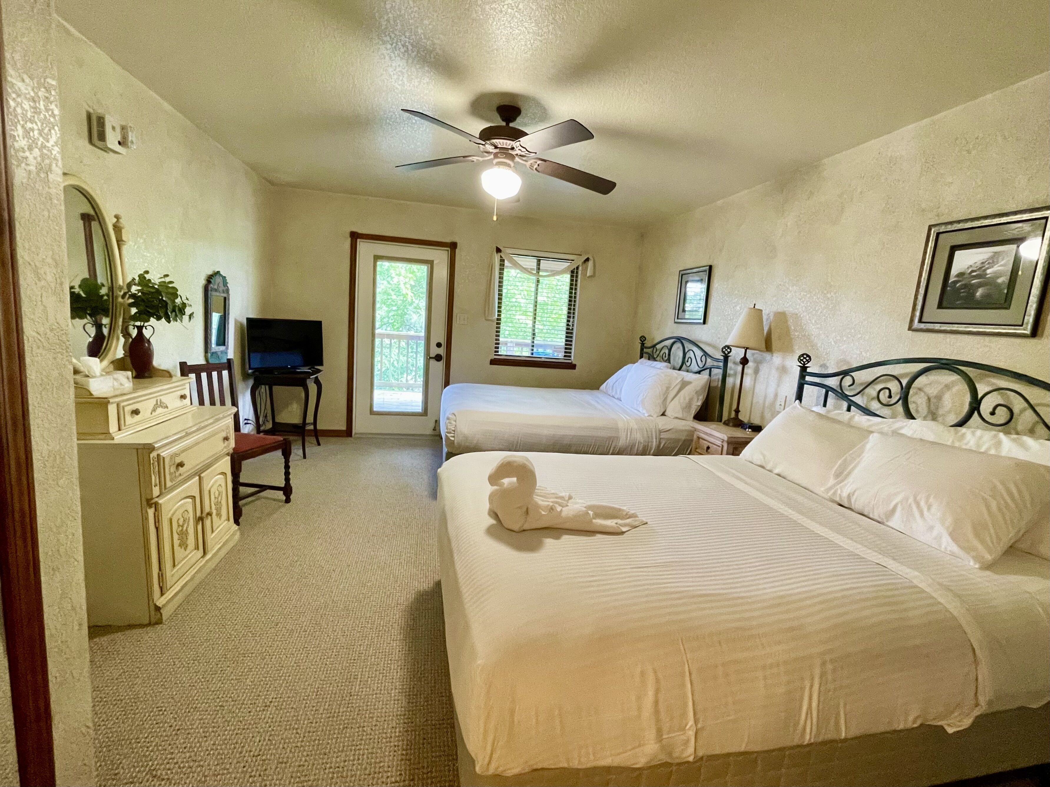 A bedroom with two beds, a ceiling fan, a dresser, a television, and a door leading to a balcony.