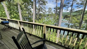 Une terrasse en bois avec un banc et un barbecue, donnant sur un lac et une zone boisée.