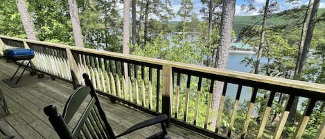 A wooden deck with a bench and a grill, overlooking a lake and forested area.