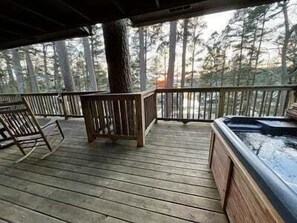 A wooden deck with a hot tub, chairs, and a view of a forest. - Mountain Harbor two bedroom Lodge cottage by RedAwning (Mount Ida)