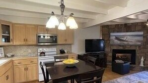 A modern kitchen with wooden cabinets, a dining table with chairs, a built-in oven, and a stone fireplace. - Mountain Harbor two bedroom Lodge cottage by RedAwning (Mount Ida)