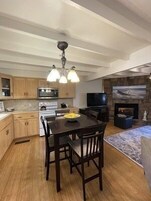 Una cocina moderna con armarios de madera, una mesa de comedor con sillas, horno empotrado y chimenea de piedra.