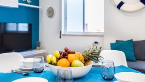 A modern living room with a dining area, featuring a fruit bowl, dining table, chairs, and a television.
