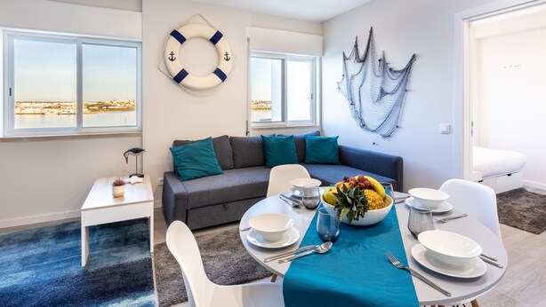 A modern living room with a sofa, dining table set for four, and a view of the city through large windows.