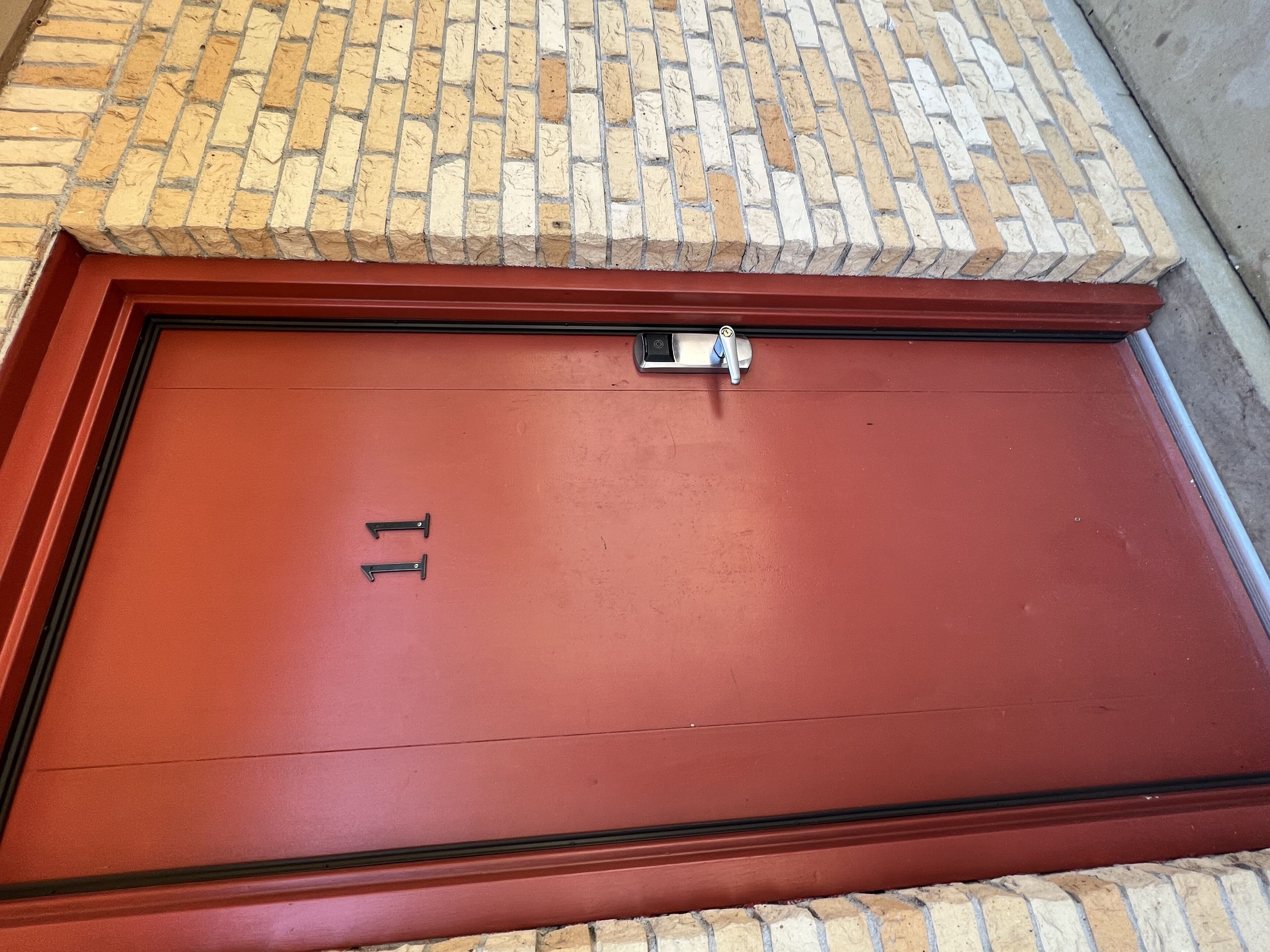 Una puerta roja con el número 11, un teclado de seguridad y una pequeña ventana encima.